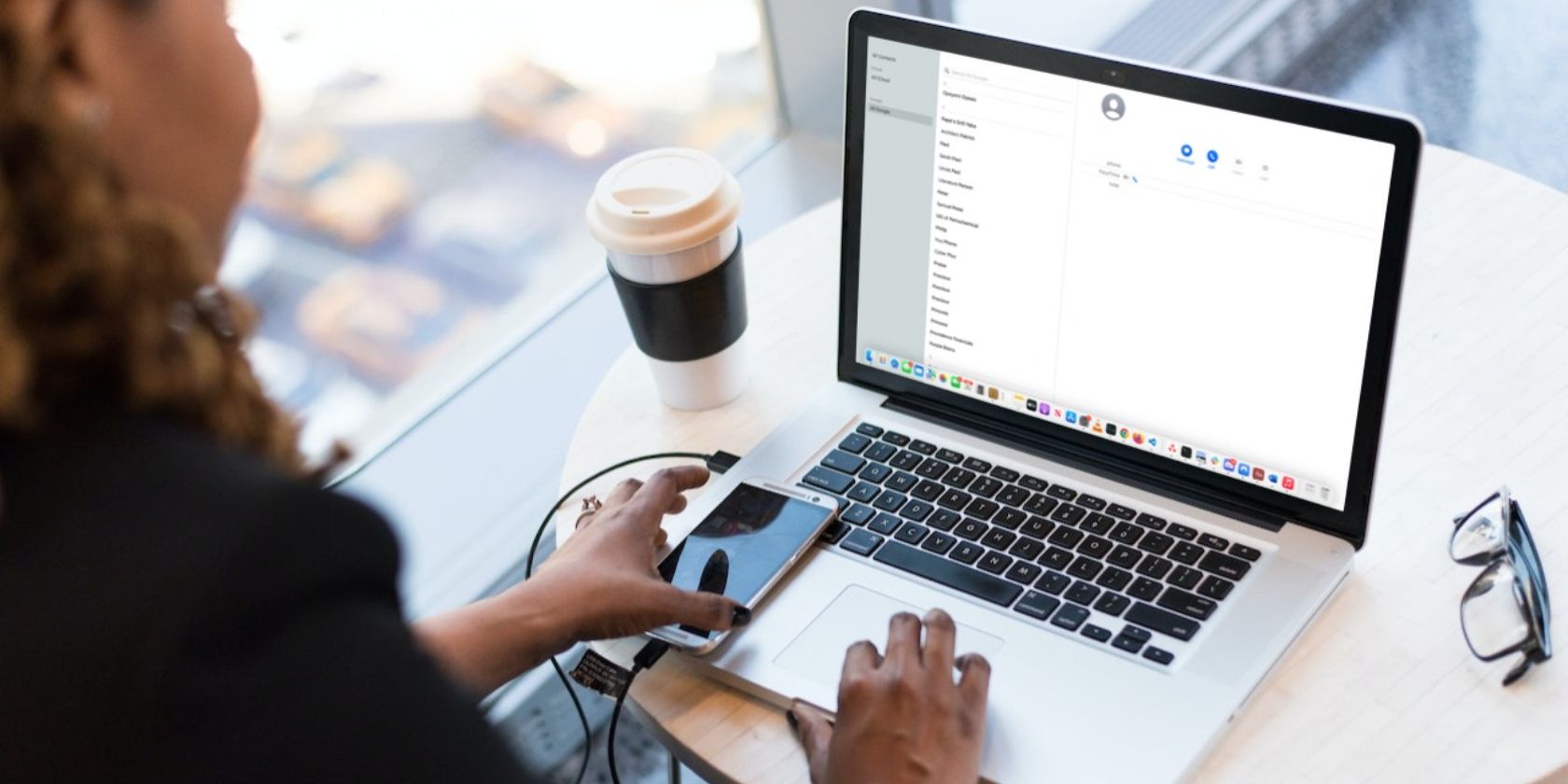 Woman using a MacBook Pro with Contacts window on-screen and a smartphone on the laptop