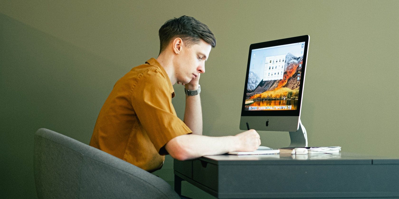 Người đàn ông viết vào sổ tay khi ngồi trước iMac