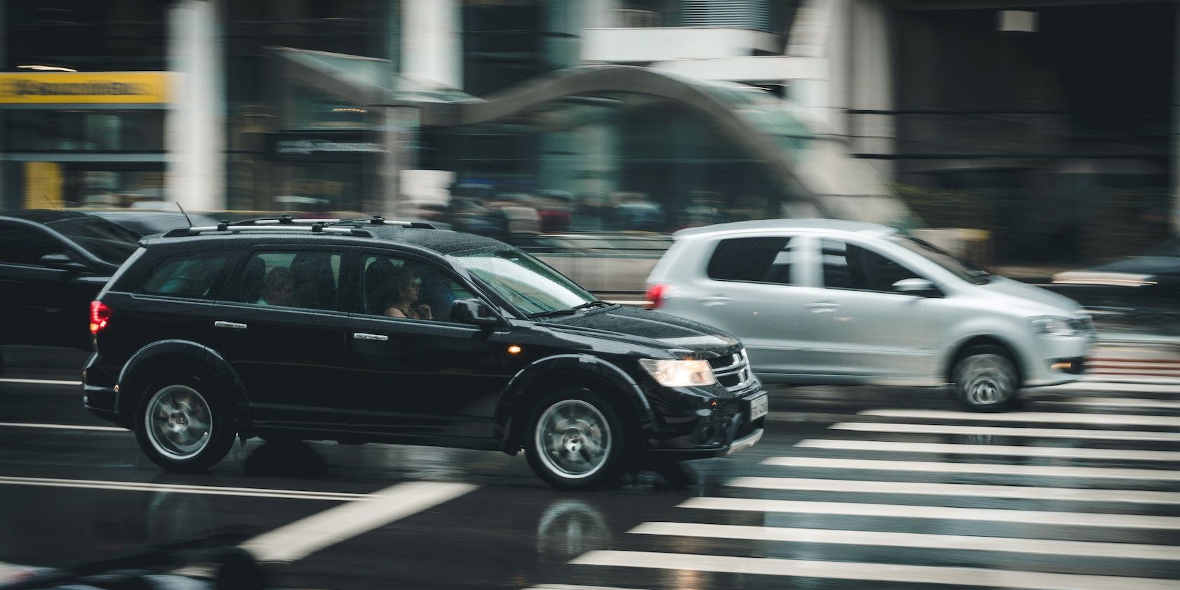 Chiếc SUV màu đen chạy dọc theo chiếc hatchback màu xám đang đến gần lối băng qua đường.