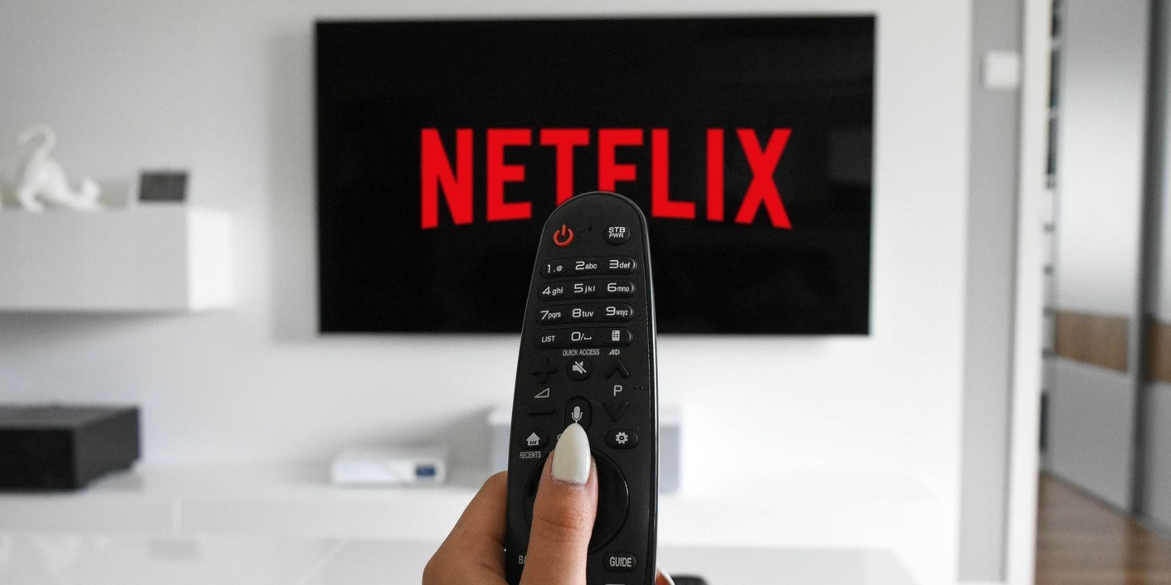 A woman holding a TV remote in front of a TV with Netflix loading up on it