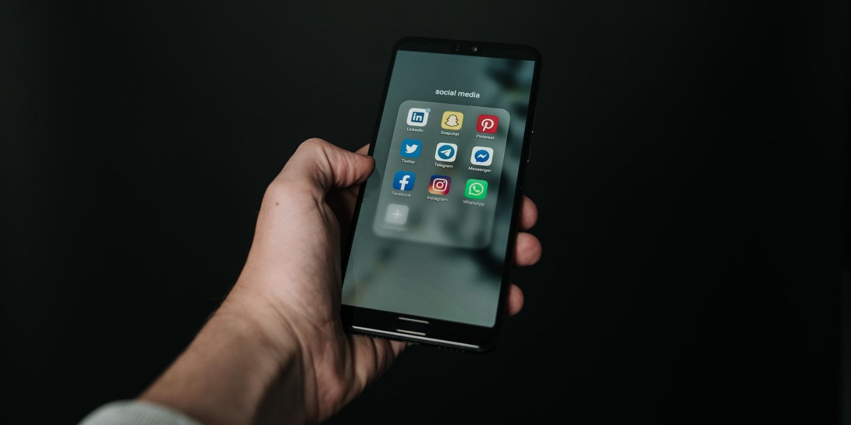 Person holding a smartphone with various social media icons showing on home screen