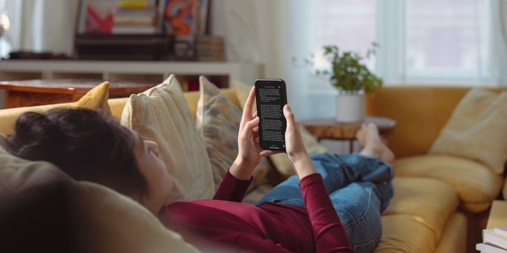 A girl lying on the couch reading a book on her iPhone